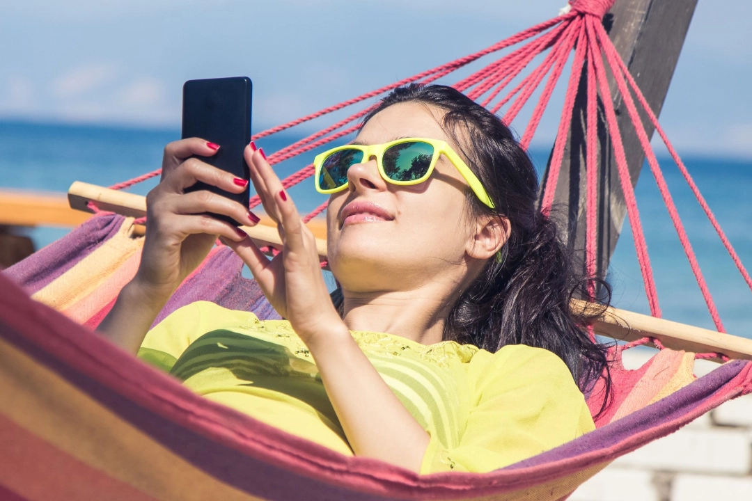 Junge Frau liegt mit ihrem Smartphone in einer Hängematte